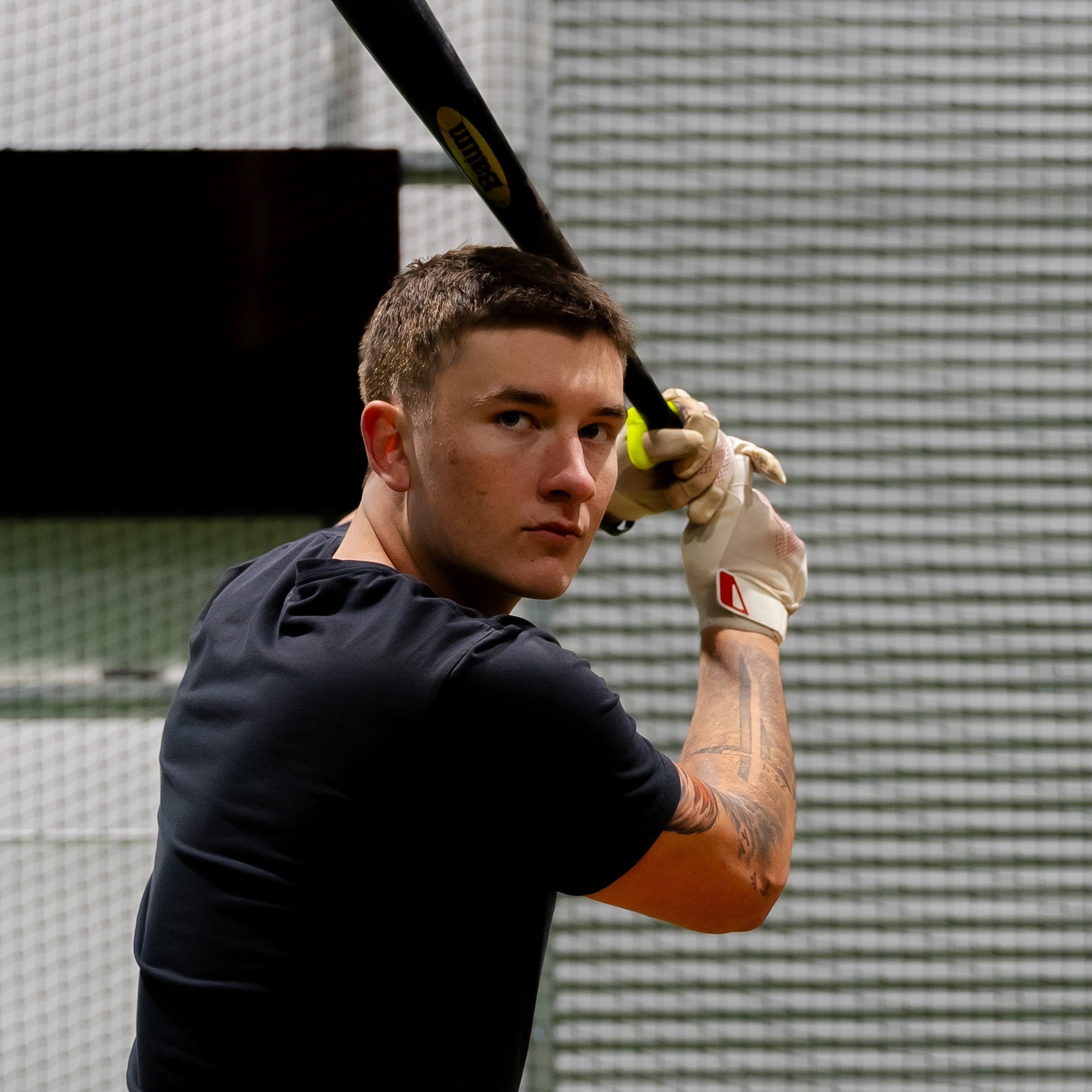 A focused baseball player grips his bat, confidently ready to swing while wearing the Hit Hero Baseball Thumb Guard. The moldable design ensures a custom fit, providing protection and performance enhancement during batting practice.