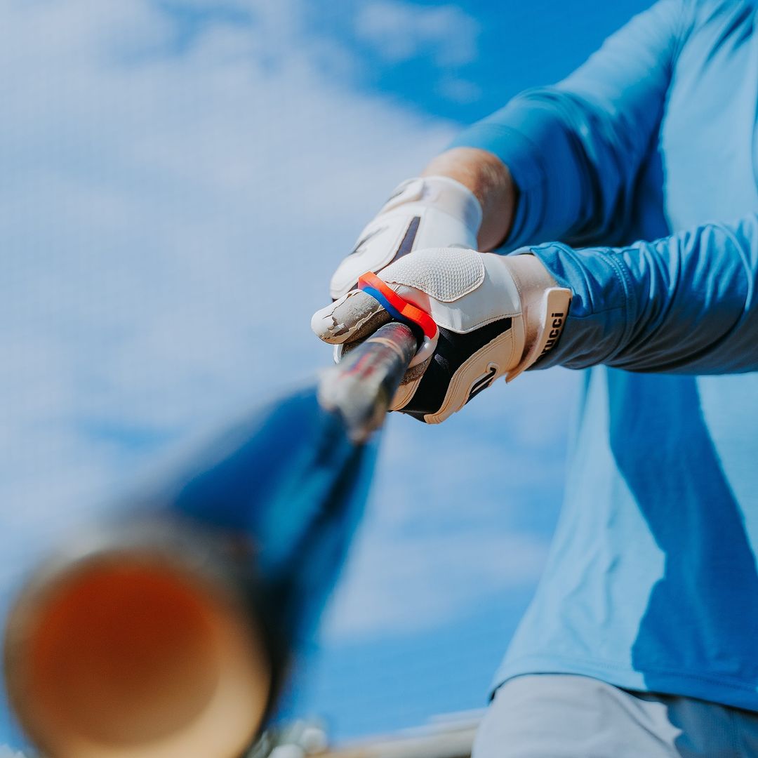Close-up of a batter gripping the bat with precision, using the Hit Hero Baseball Thumb Guard. The moldable thumb guard offers custom-fit protection, ensuring maximum comfort and performance under the blue sky