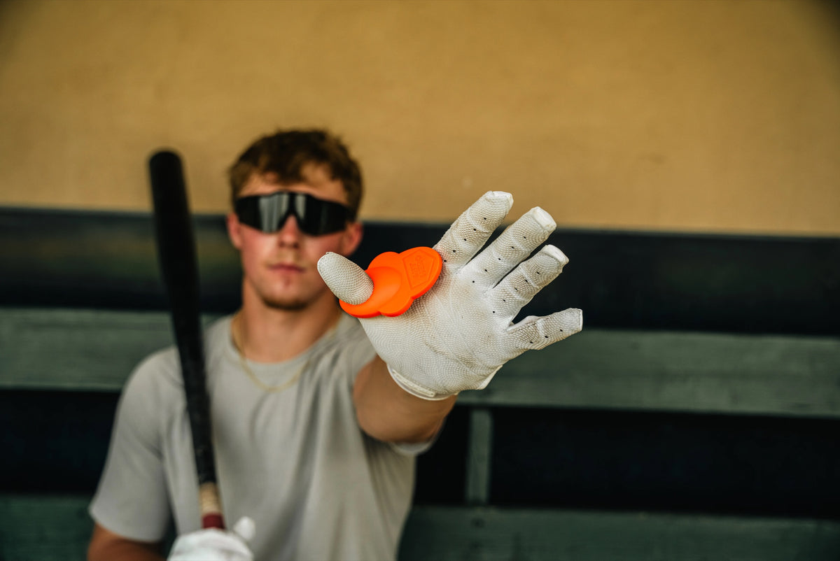 Hit Hero orange guard worn on the thumb gripping a bat