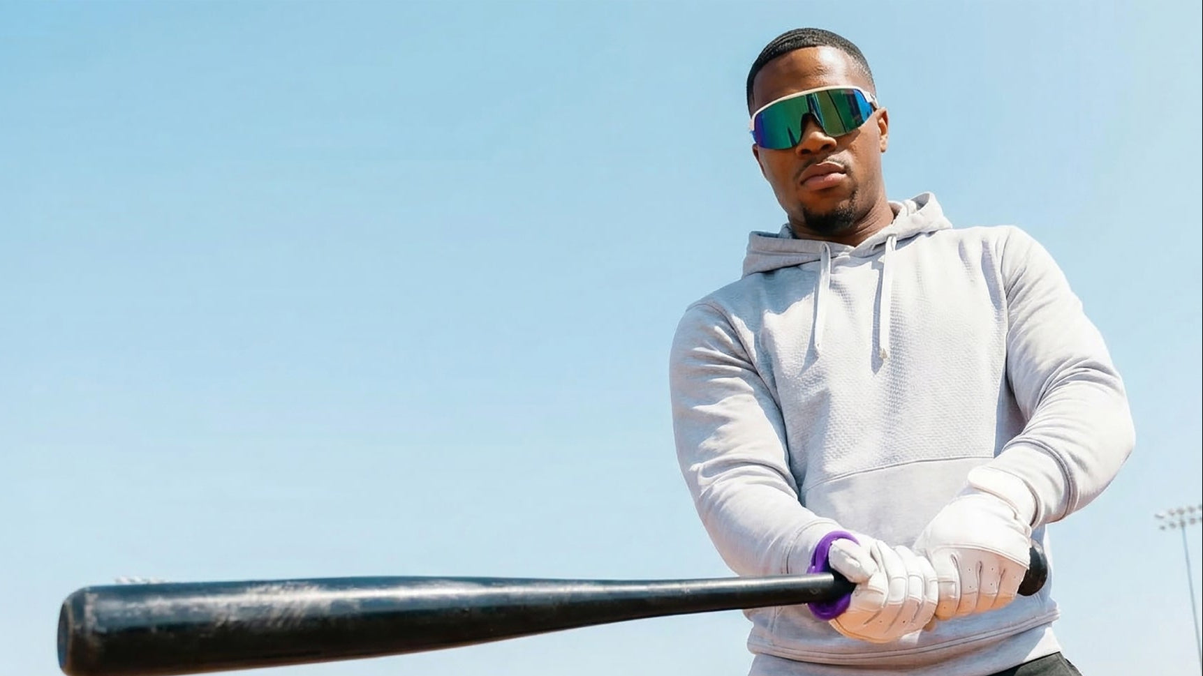 Person holding a baseball bat against a clear blue sky wearing a purple hit hero
